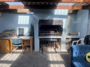 Un espacio exterior cubierto con una parrilla, una mesa con sillas y un sofá azul.