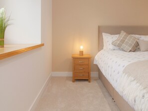 A bedroom with a bed, bedside table, and a nightstand with a lamp. - The Cottage by Interhome (Lossiemouth)