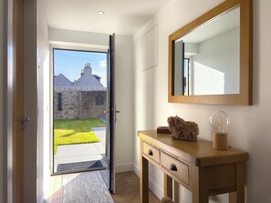 A room with a wooden dresser, a mirror, and a view of a garden and buildings outside. - The Cottage by Interhome (Lossiemouth)