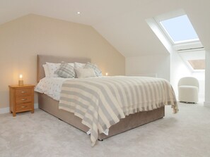 Een slaapkamer met een schuine hemel, een bed met gestreept beddengoed, een nachtkastje met een lamp en een dakvenster.