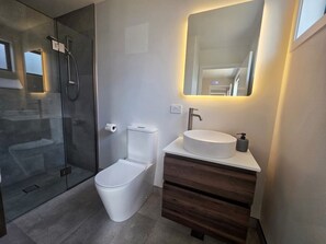 A modern bathroom with a glass shower enclosure, a toilet, a sink with a mirror, and wooden cabinetry. - Kernel Retreat
Relax in our tranquil guest house and dedicated car park. (Jack's Point)
