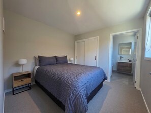 A bedroom with a bed, bedside tables, a wardrobe, and a bathroom visible through an open door. - Kernel Retreat
Relax in our tranquil guest house and dedicated car park. (Jack's Point)