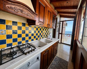 Una cocina con estufa a gas, lavamanos, armarios de madera y salpicadero de azulejos.