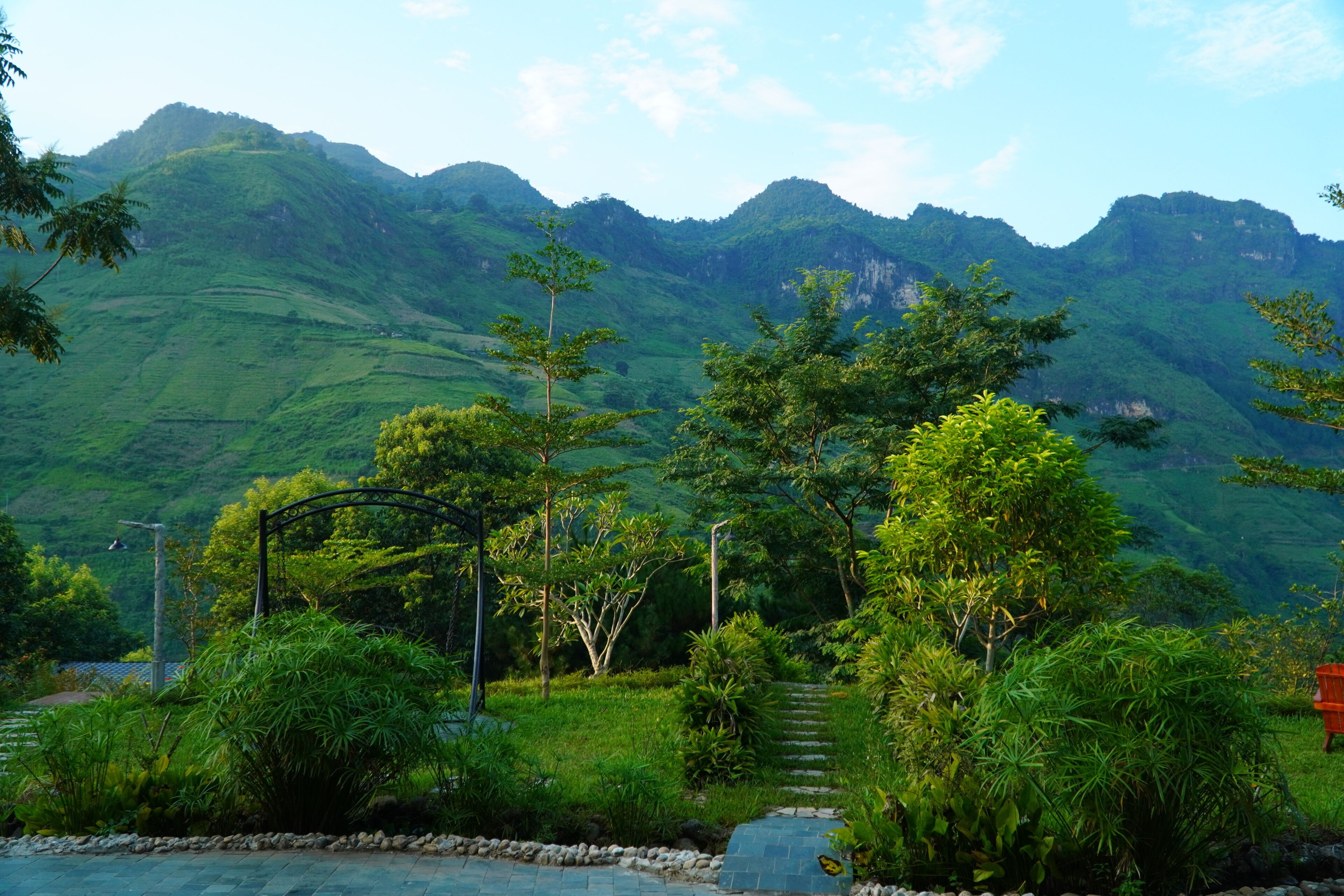 Un paysage montagneux, avec une végétation luxuriante et un sentier de pierres qui traverse un jardin.