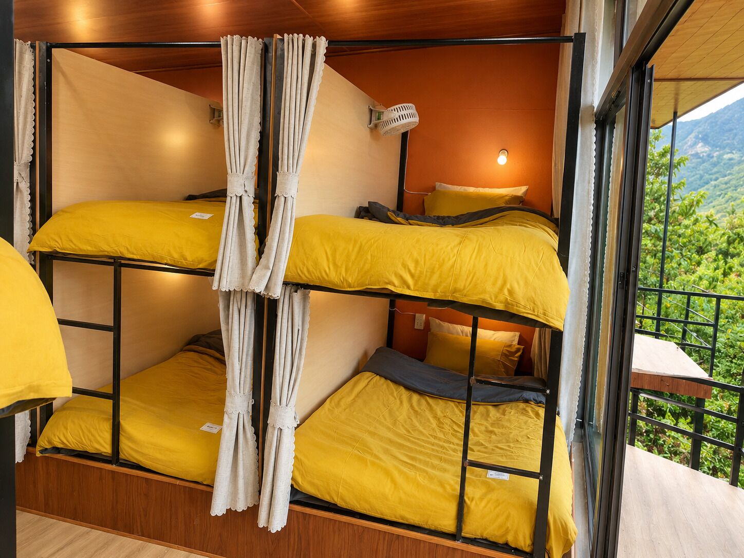 Ein Stockbett mit gelber Bettwäsche und weißen Vorhängen, ein Holzboden und Blick ins Grüne.