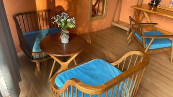 A room with a round wooden table, two wooden chairs with blue cushions, a vase with flowers, and a coffee machine on a wooden shelf.