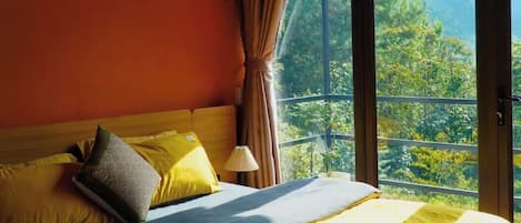 Cama com vista para uma paisagem montanhosa através de grandes janelas.