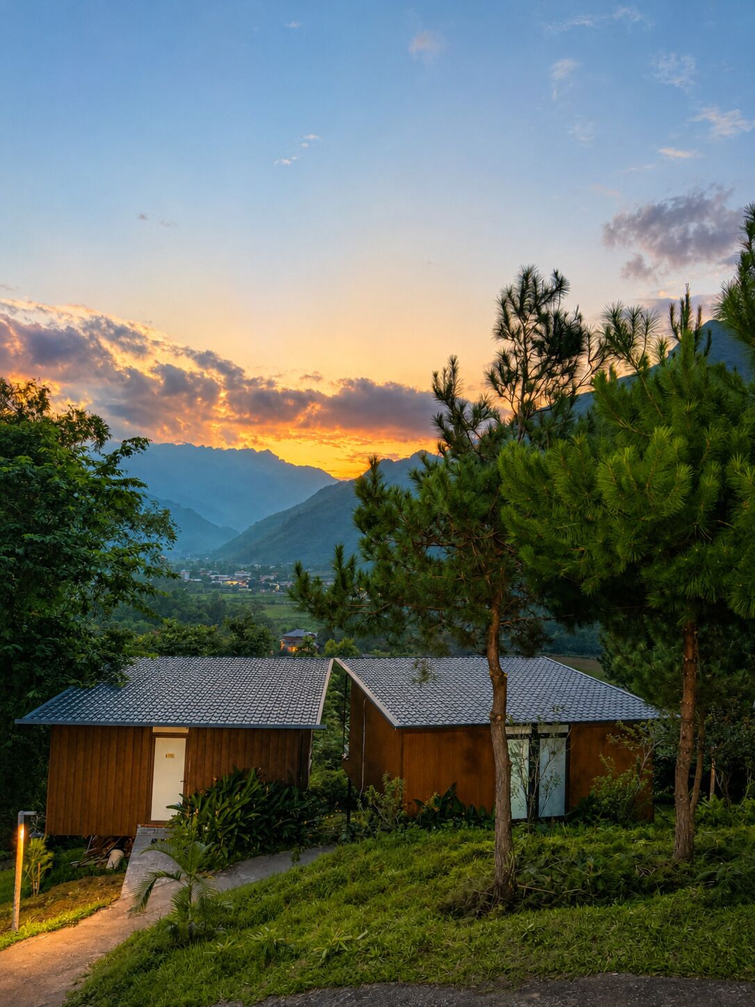 A rustic cabin with a sloped roof, surrounded by lush greenery and a mountainous backdrop.