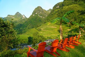 Vista de un paisaje montañoso con un río, abundante vegetación y sillas de madera rojas.