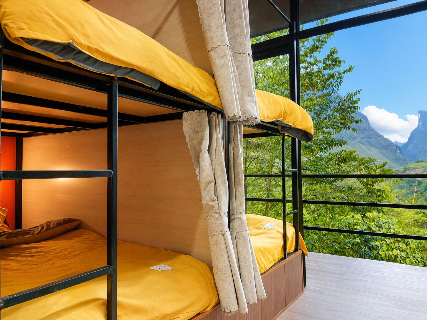 A bunk bed with yellow bedding and a view of green foliage and mountains through a window.