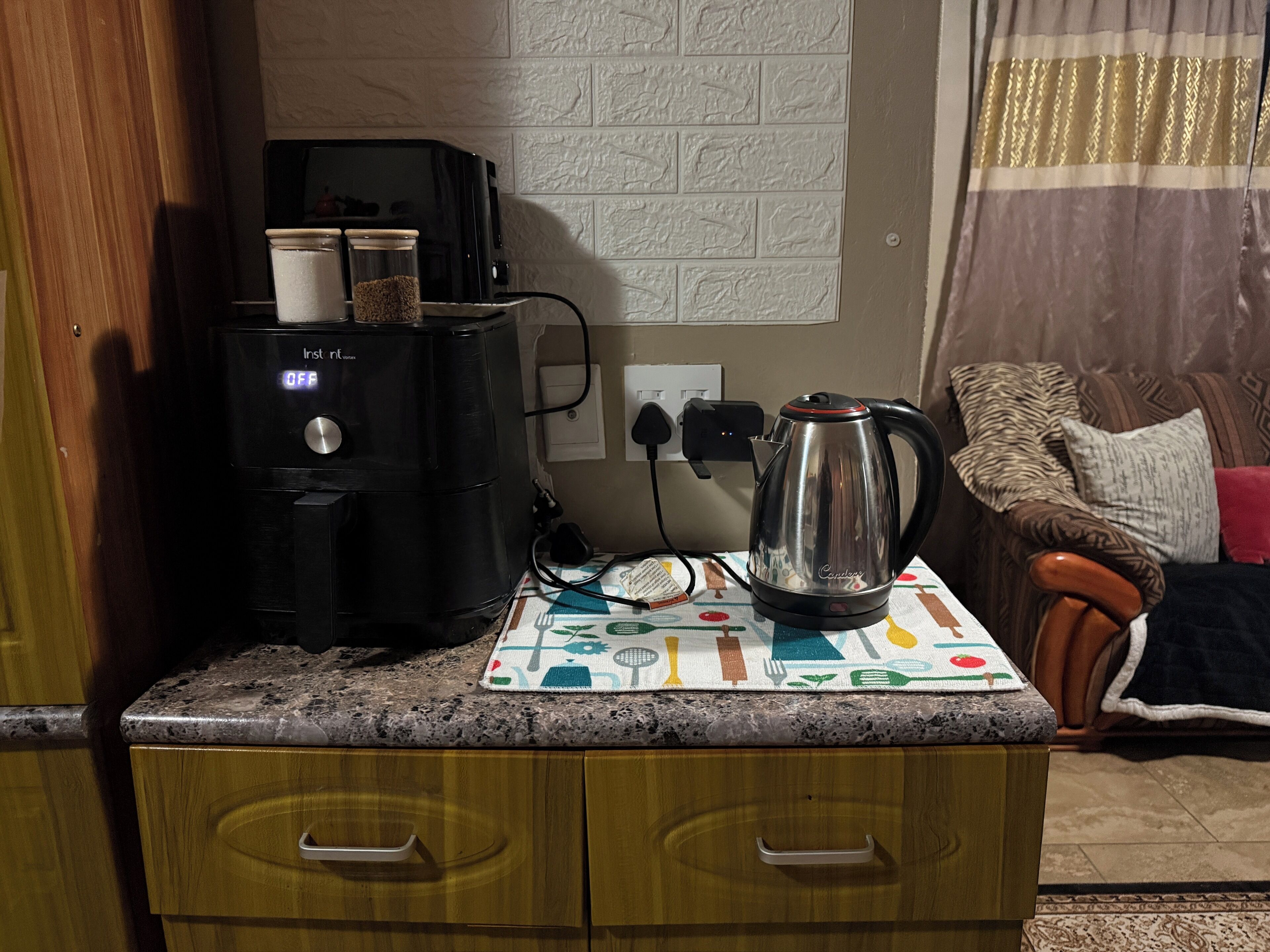 Una encimera de cocina con cafetera, hervidor y microondas. Debajo, un mueble de madera.