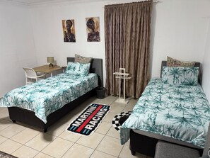 Una habitación con dos camas, un escritorio, una silla, una lámpara y dos obras de arte en la pared.