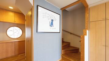 A hallway with a framed artwork, wooden flooring, a staircase, and a round window.