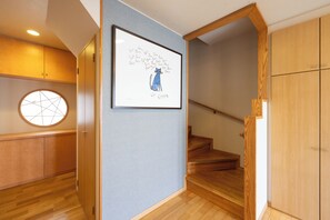 A hallway with a framed artwork, wooden flooring, a staircase, and a round window.