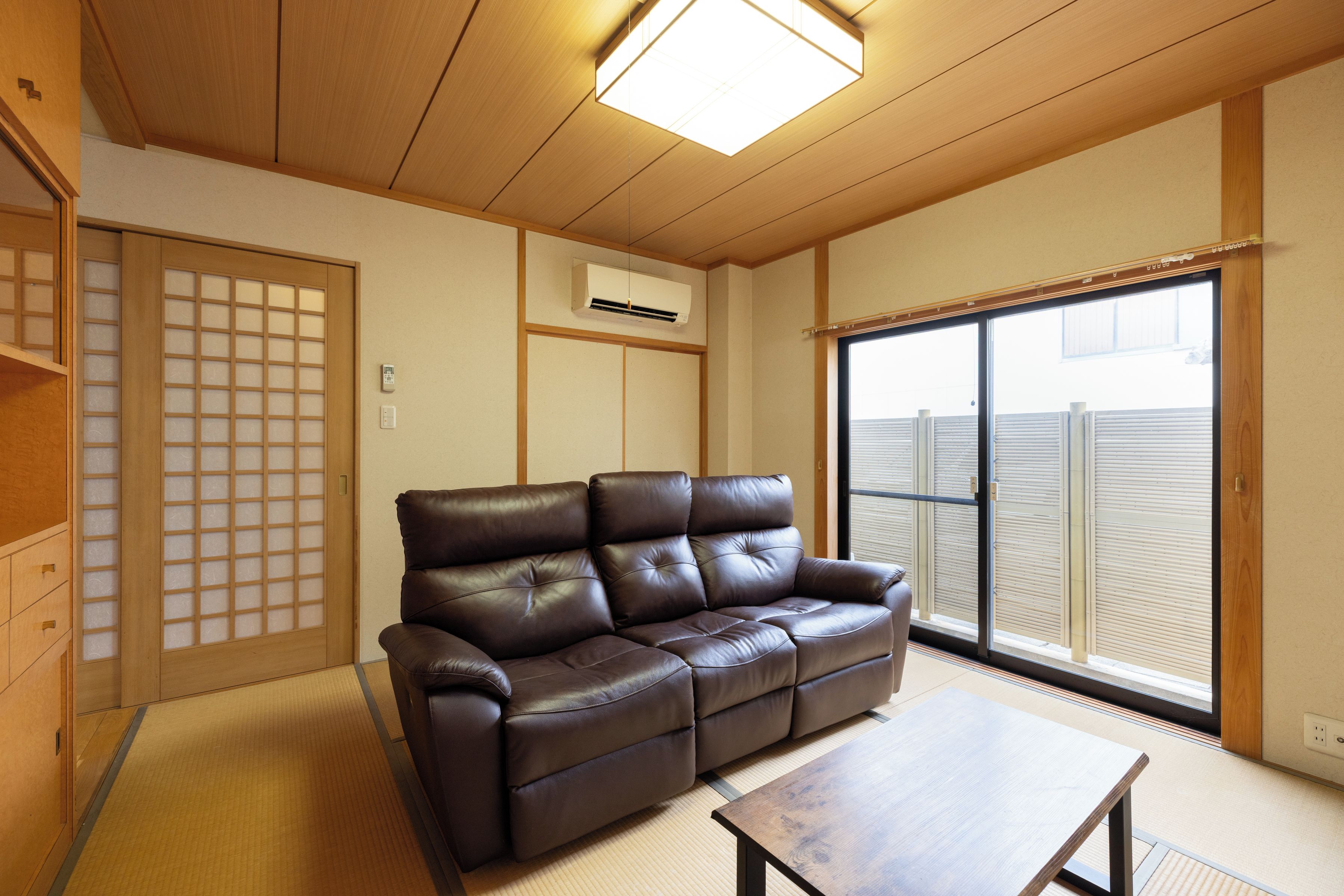 A living room with a brown leather sofa, a wooden coffee table, and a sliding glass door leading to a balcony.
