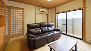 Ein Wohnzimmer mit einem braunen Ledersofa, einem Holztisch und einer Glasschiebetür, die auf einen Balkon führt.