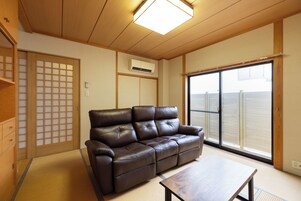A living room with a brown leather sofa, a wooden coffee table, and a sliding glass door leading to a balcony.