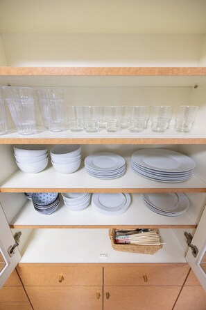 A kitchen with white cabinets, shelves with clear drinking glasses, white plates, and bowls.