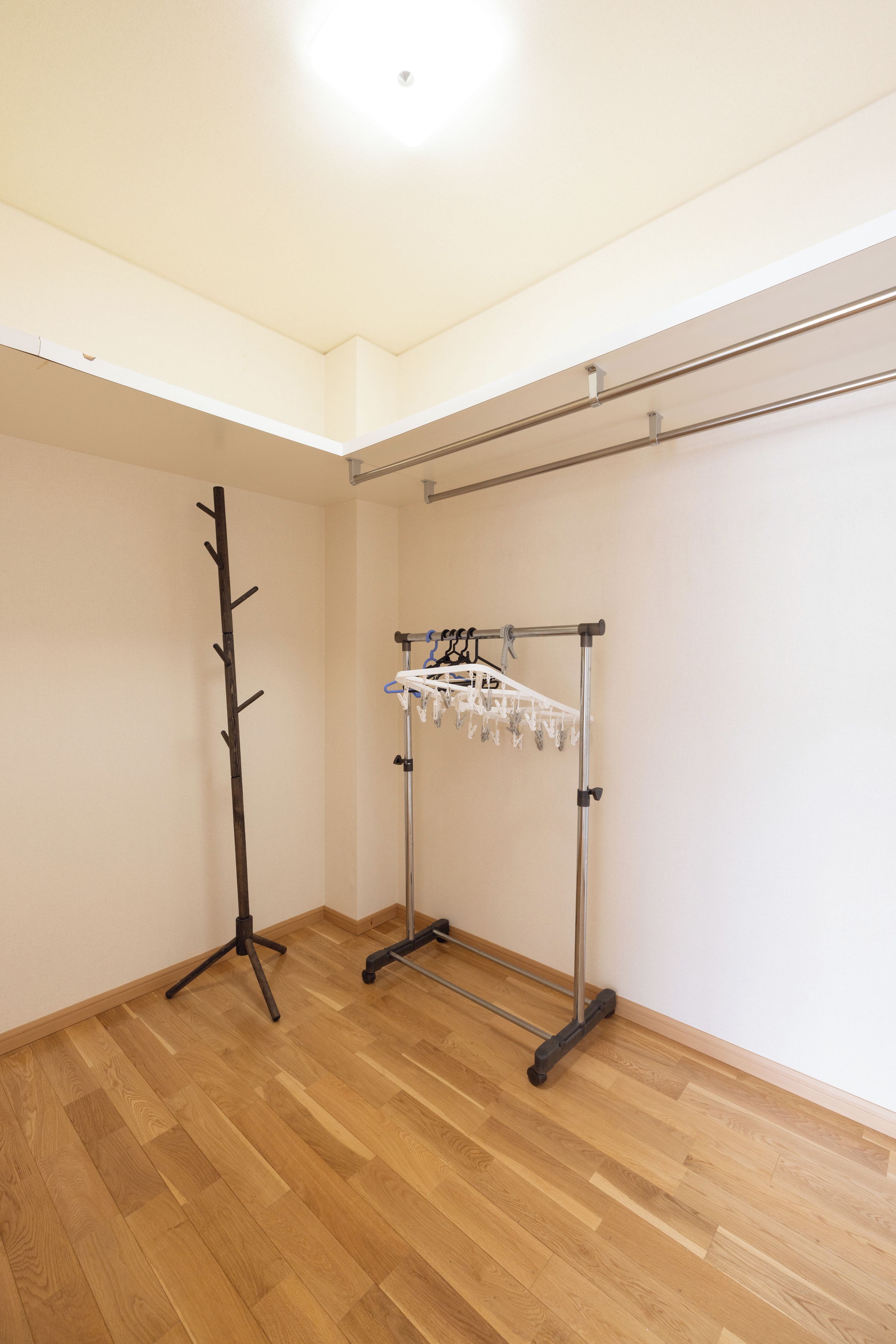A room with a wooden floor, a coat rack, and a metal drying rack.