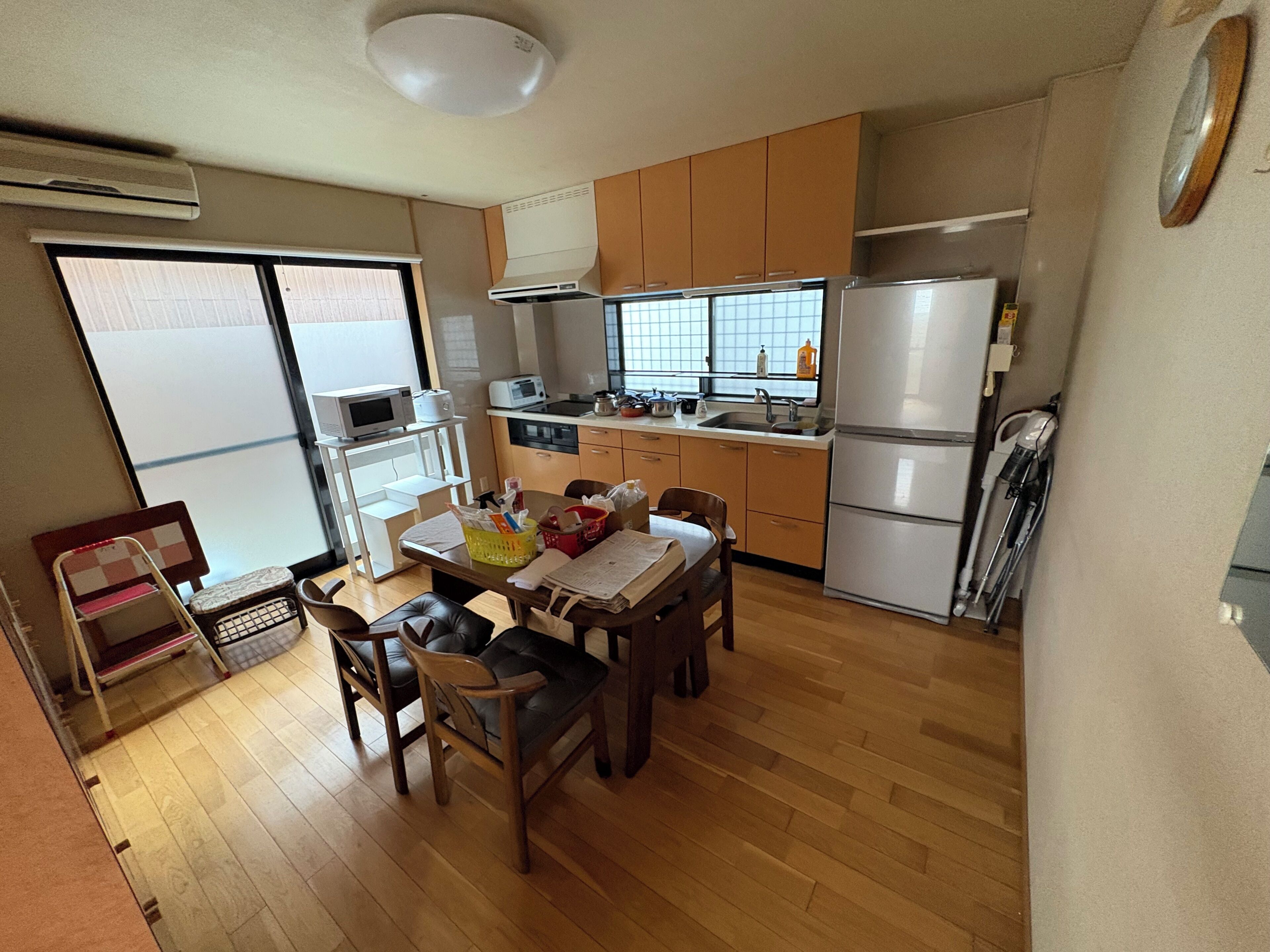 Cozinha compacta com área de refeições, piso de madeira e vista através de uma porta deslizante.