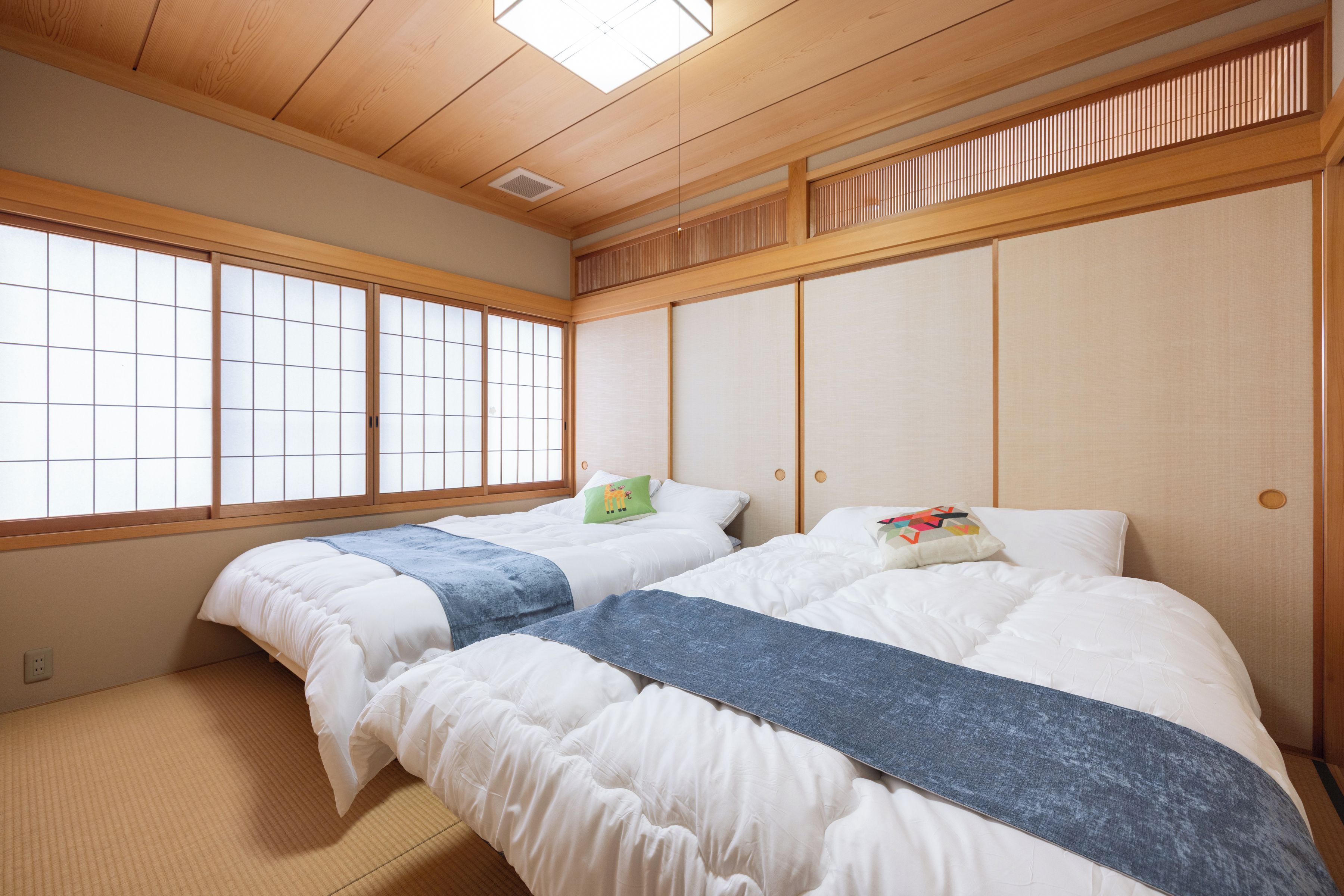 A traditional Japanese-style room with tatami flooring, two beds with white bedding and blue blankets, and a shoji screen door.