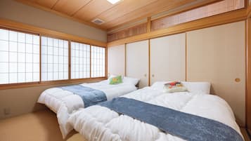 A traditional Japanese-style room with tatami flooring, two beds with white bedding and blue blankets, and a shoji screen door.
