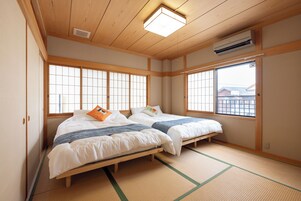 Una habitación tradicional japonesa con suelo de tatami, dos camas con ropa blanca y ventanas grandes con paneles shoji.