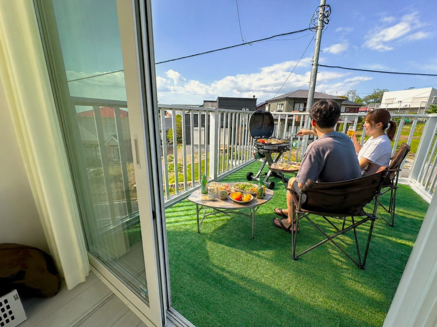 Un balcon avec un barbecue, une table garnie de nourriture et une vue sur le quartier.