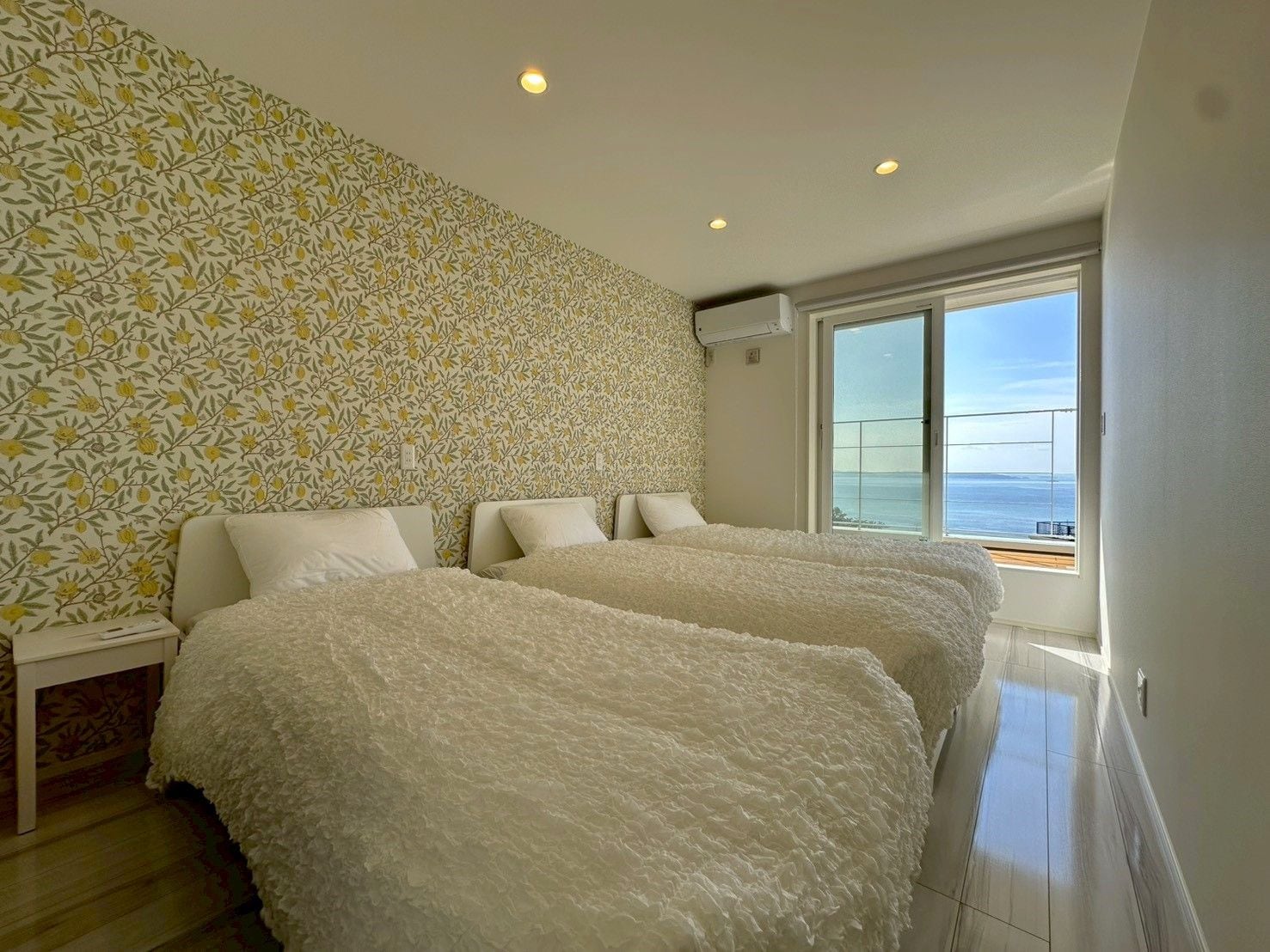A bedroom with two beds, a patterned wall, and a balcony with a view.