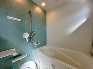 Ein Badezimmer mit einer Badewanne, einer Duschbrause, einem am Wand montierten Wasserhahn, einem Handwaschbecken und einer Toilette.
