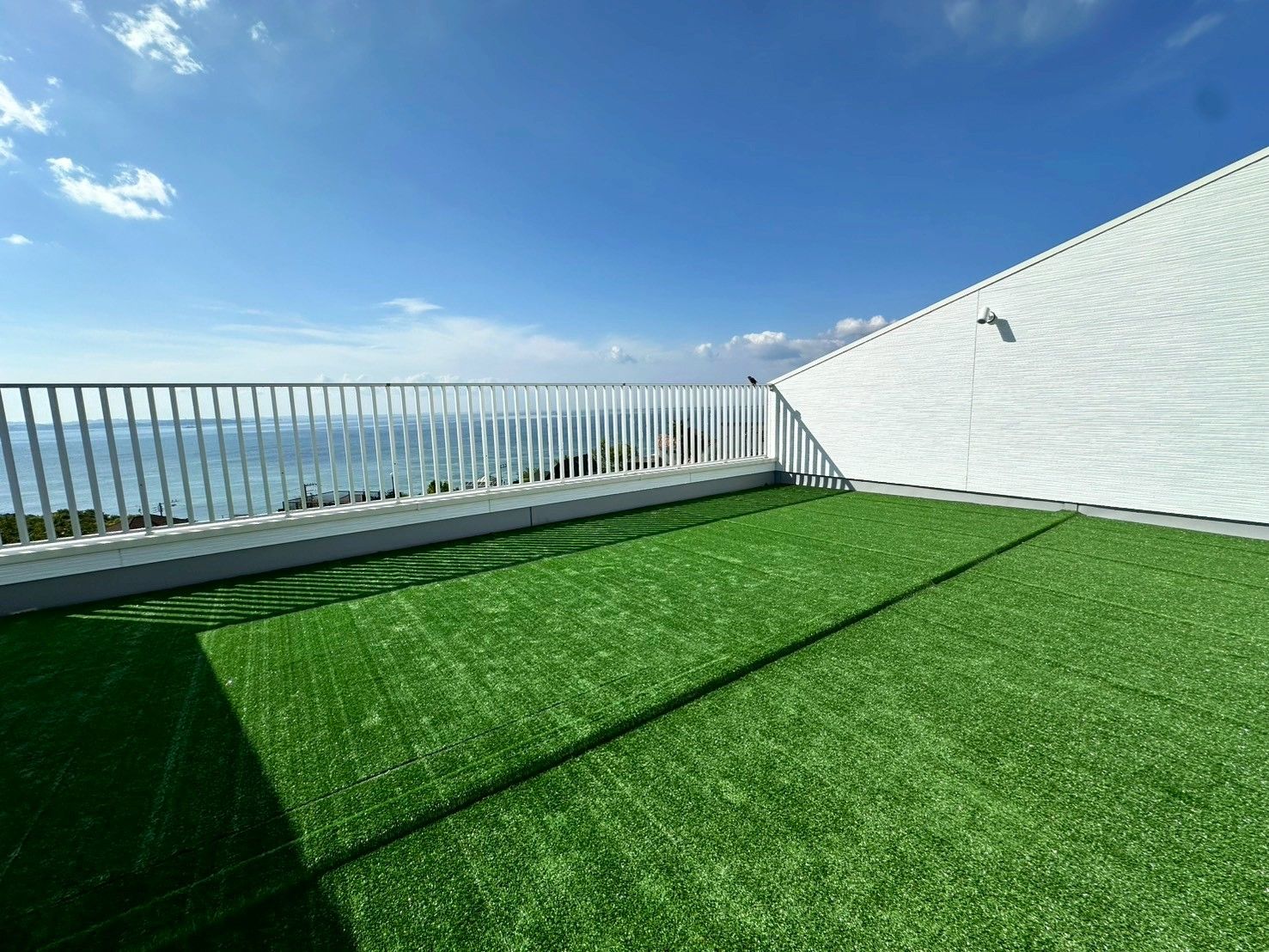 Une terrasse sur le toit offrant une vue sur la mer, avec une balustrade blanche et un revêtement de sol en gazon synthétique.