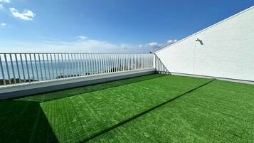 Une terrasse sur le toit offrant une vue sur la mer, avec une balustrade blanche et un revêtement de sol en gazon synthétique.
