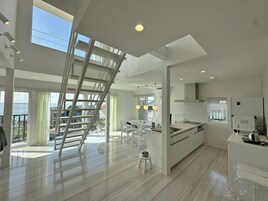 Una cocina moderna con una isla central, una zona de comedor con una mesa alta y una escalera que conduce a un nivel superior.
