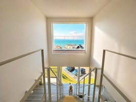 Una escalera conduce a un balcón con vista al mar y edificios.