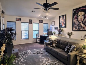 A living room with a grey sofa, patterned rug, ceiling fan, and artwork on the walls.