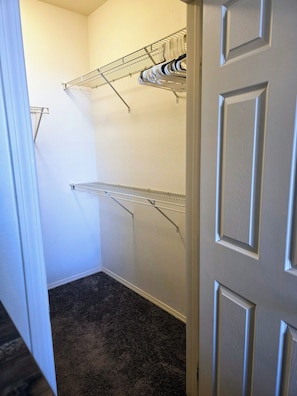 Un couloir étroit, doté d’un sol recouvert de moquette, d’une porte blanche et de deux étagères en fil de métal adossées au mur.