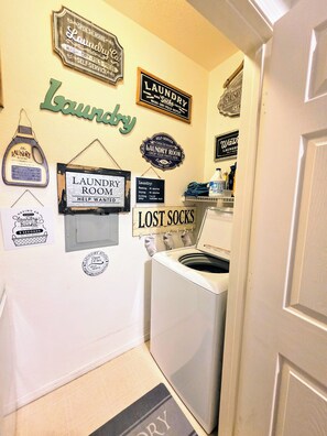 A laundry room with a washing machine, a sink, and various laundry-related signs on the wall.