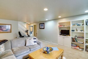 A living room with a gray sofa, a coffee table with a bowl, a staircase, and a bookshelf with various items. - Near Universities & Hospitals! SLC Home w/ Yard (Salt Lake City)