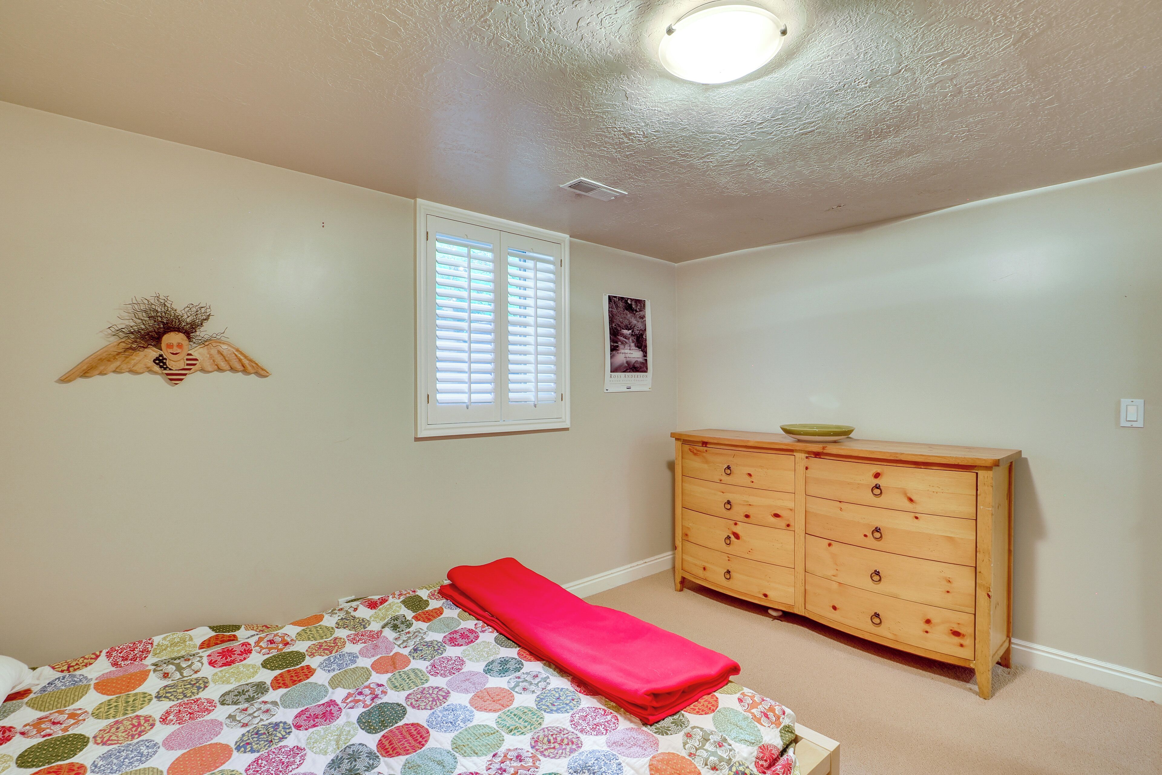 A bedroom with a bed, a dresser, a window with blinds, and a wall decoration.