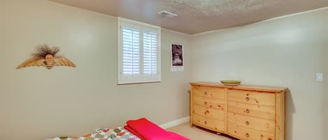 Quarto com cama, penteadeira, janela com persianas e um objeto decorativo na parede.
