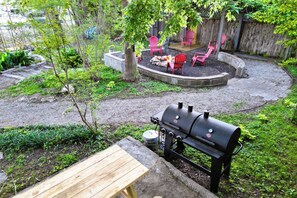 Un patio trasero con una parrilla, sillas rojas y una mesa de madera.