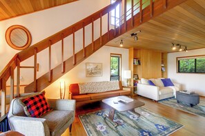A spacious living area with a wooden staircase, a sofa, a coffee table, and a bookshelf. - Hood Canal Views & Near Alderbrook Resort! (Union)