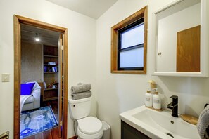 Ein Badezimmer mit Toilette, Waschbecken und einem Fenster. Ein Regal mit Pflegeprodukten und ein Teppichboden sind ebenfalls vorhanden.