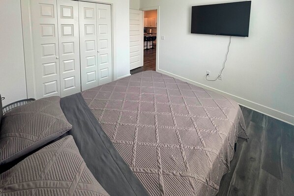 A bedroom with a bed, a TV mounted on the wall, and a closet with sliding doors.