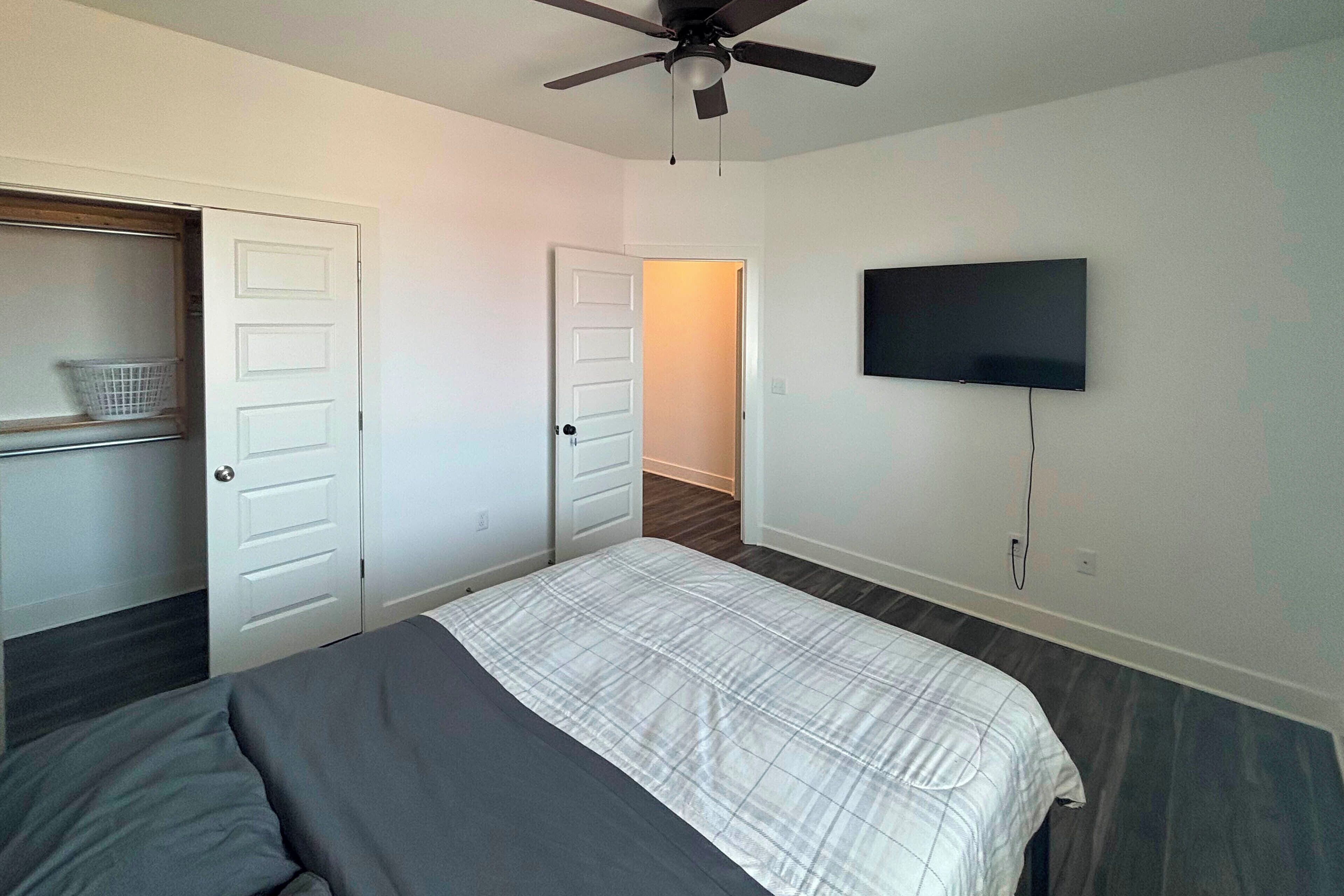 A bedroom with a bed, a ceiling fan, a TV mounted on the wall, and a closet with a basket.