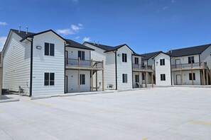 A row of two-story buildings with balconies, a parking lot, and a clear sky.