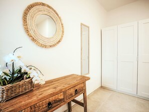 Un armari de fusta amb calaixos, un mirall de vimetga i una cistella de vimetga amb orquídies blanques.