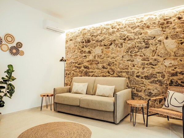 A modern living room with a stone wall, a beige sofa, a round coffee table, and a wicker chair.