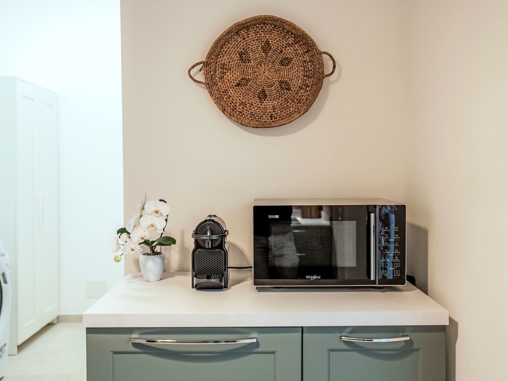 A kitchen with a microwave, a coffee maker, and a potted orchid on the counter.