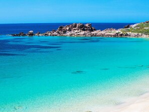 A coastal landscape with clear turquoise waters, rocky formations, and a sandy beach.